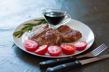 Biberiyeli, domatesli ve soslu, koyu beton bir arka planda, mis kokulu biftek, biftek veya domuz eti.