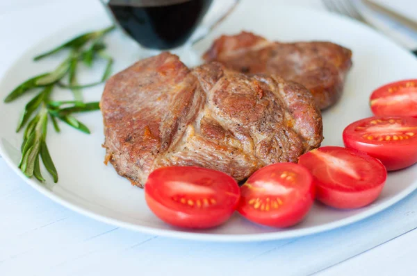 Ízletes, lédús, sült hússteak sertéshúsból vagy marhahús szósszal, fűszerekkel és paradicsommal szürke tálcán, könnyű háttérrel — Stock Fotó