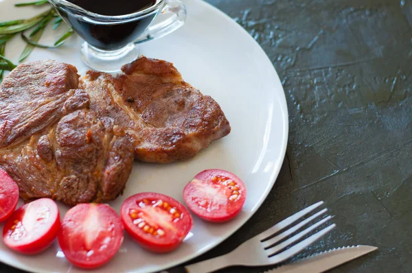 Filetes de carne jugosa de ternera, ternera o cerdo con romero, tomates y salsa, en plato gris, sobre un fondo de hormigón oscuro con espacio para copiar —  Fotos de Stock