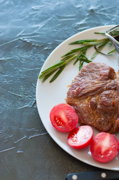 Bifes de carne perfumados e suculentos de vitela, carne bovina ou suína com alecrim, tomate e molho, em prato cinza, em fundo de concreto escuro, formato vertical — Fotografia de Stock