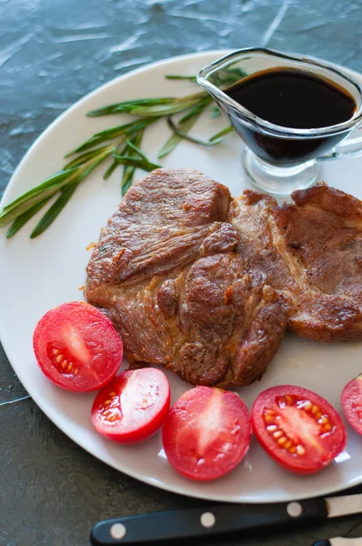 Bistecche di carne profumate e succose di vitello, manzo o maiale con rosmarino, pomodori e salsa, su piatto grigio, su fondo di cemento scuro, formato verticale — Foto Stock