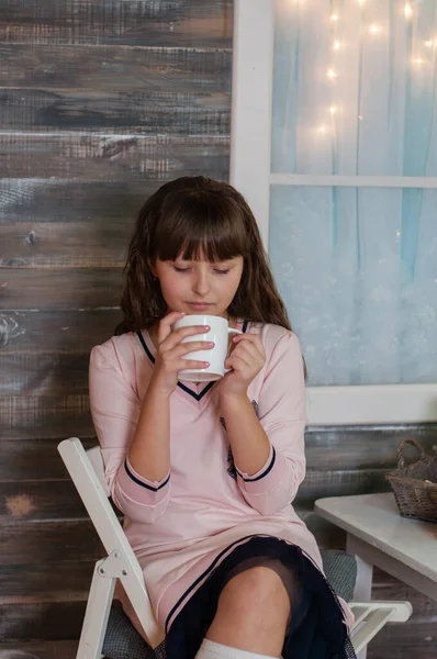 Hermosa chica adolescente en un vestido con una taza de té en la mesa, mira en la taza —  Fotos de Stock