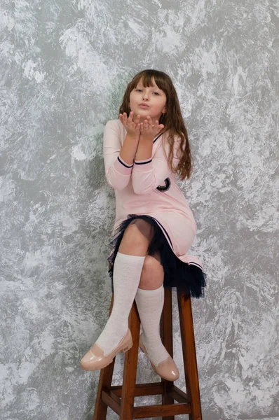 Hermosa niña adolescente envía un beso. Chica sentada en una silla contra una pared gris —  Fotos de Stock