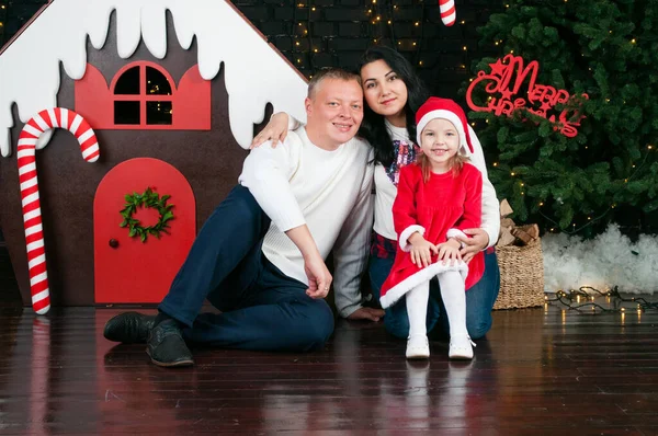 Happy, contented, smiling family. Dad, mom and daughter near the New Year tree. — Stock Photo, Image