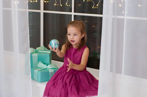 Petite fille très mignonne jouant avec le ballon du Nouvel An. Fille en robe assis sur le rebord de la fenêtre — Photo