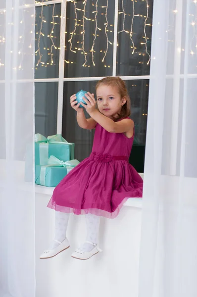 Petite fille très mignonne jouant avec le ballon du Nouvel An. Fille en robe assis sur le rebord de la fenêtre — Photo