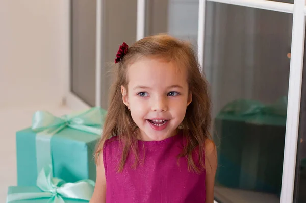 Menina sorridente bonito com presentes de Natal sentado no peitoril da janela. Ri e olha para o outro lado — Fotografia de Stock