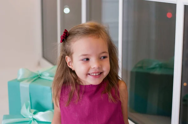 Menina sorridente bonito com presentes de Natal sentado no peitoril da janela. Ri e olha para o outro lado — Fotografia de Stock