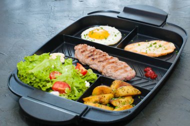 Kahvaltı, pirzola ya da biftek, domates salatası, kızarmış patates, kızarmış ekmek ve siyah tabakta kızarmış yumurta. Restoranda öğle yemeği servis ediliyor..