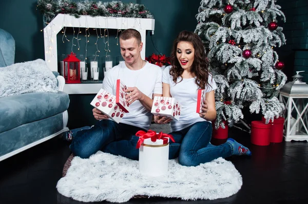 快乐快乐的年轻夫妇在壁炉边和圣诞树旁 惊喜地打开礼物 — 图库照片