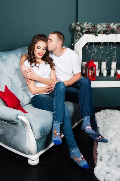 一对有爱心的已婚夫妇 一个苗条的 有运动能力的男人和一个漂亮的女人在靠近壁炉的沙发上的圣诞内饰 丈夫亲吻他的妻子 — 图库照片