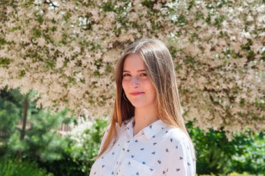 İnanılmaz güzel bir kızın güneşli portresi. Bir yaz günü çiçek açan ağacın yanında.