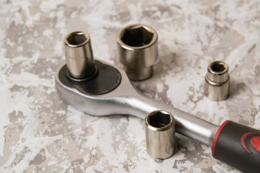 Çıngıraklı eski İngiliz anahtarı ve gri macunun arka planında farklı başlıklar.