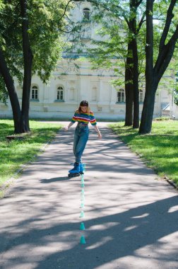 Güzel kız yazın parkta paten kayarken, vyponyaet numaraları yaparken ve çipleri gezerken eğleniyor..