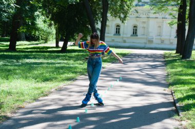 Güzel kız yazın parkta paten kayarken, vyponyaet numaraları yaparken ve çipleri gezerken eğleniyor..