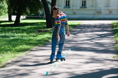 Güzel kız yazın parkta paten kayarken, vyponyaet numaraları yaparken ve çipleri gezerken eğleniyor..