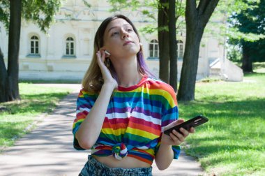 Kulaklıklı çok güzel bir kız, şehir parkında akıllı bir telefonla müzik dinliyor ya da konuşuyor.