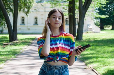 Kulaklıklı çok güzel bir kız, şehir parkında akıllı bir telefonla müzik dinliyor ya da konuşuyor.