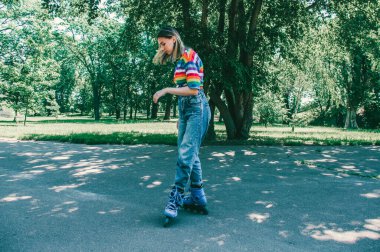 Güzel genç kız yaz günü parkta paten kayarak numaralar yapıyor.