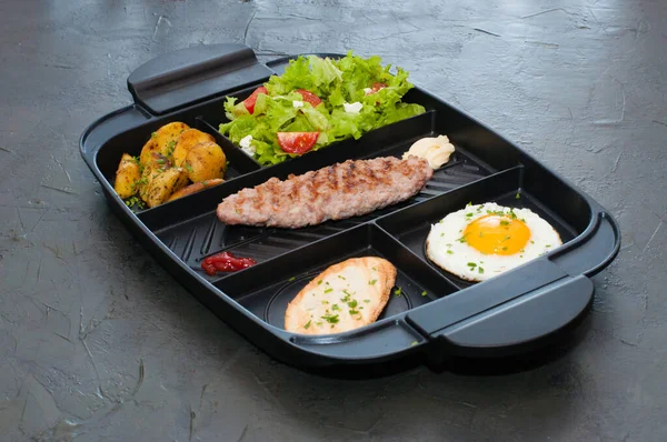 Kahvaltı, pirzola ya da biftek, domates salatası, kızarmış patates, kızarmış ekmek ve siyah tabakta kızarmış yumurta. Restoran yemeği, site için içerik