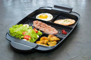 Kahvaltı, pirzola ya da biftek, domates salatası, kızarmış patates, kızarmış ekmek ve siyah tabakta kızarmış yumurta. Restoranda öğle yemeği servis ediliyor..