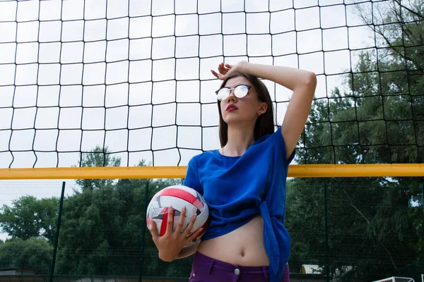 漂亮的女人 欧洲人 太阳镜 在网球场附近的沙滩排球场上摆着一个球 — 图库照片