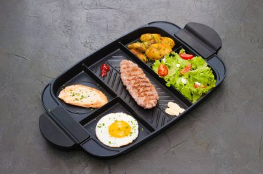 Kahvaltı, biftek ya da pirzola, domatesli ve yeşil sebzeli salata, tost, patates, siyah tabakta yumurta. Sağlıklı beslenme, diyet, menü, yüksek kalite öğle yemeği konsepti.