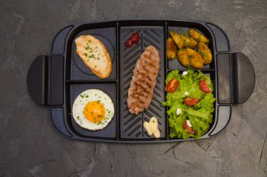 Kahvaltı, biftek ya da pirzola, domatesli ve yeşil sebzeli salata, tost, patates, siyah tabakta yumurta. Sağlıklı beslenme, diyet, menü, iyi beslenme.