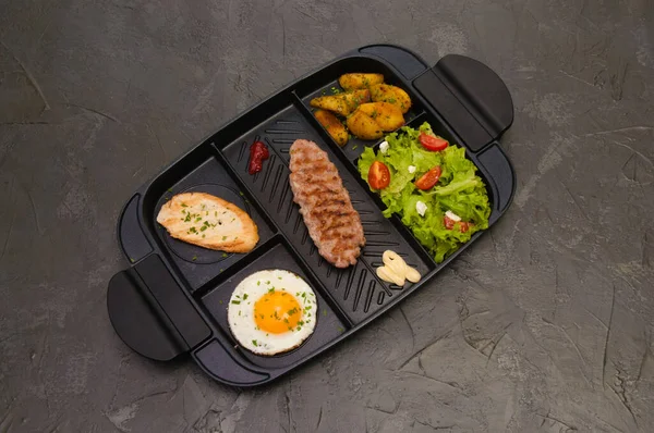 Kahvaltı bifteği ya da pirzola, domatesli ve yeşil sebzeli salata, kızarmış ekmek, patates, yumurta, üstten manzara, koyu arka plan. Sağlıklı beslenme, beslenme, menü, besleyici gıdalar.