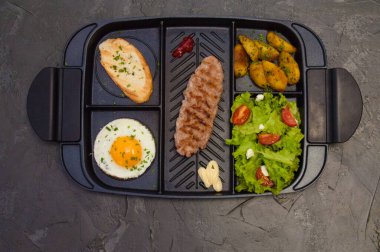 Kahvaltı, biftek ya da pirzola, domatesli ve yeşil sebzeli salata, tost, patates, siyah tabakta yumurta. Sağlıklı beslenme, diyet, menü, iyi beslenme.