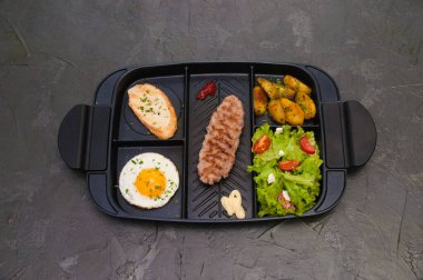 Kahvaltı bifteği ya da pirzola, domatesli ve yeşil sebzeli salata, kızarmış ekmek, patates, yumurta, üstten manzara, koyu arka plan. Sağlıklı beslenme, beslenme, menü, besleyici gıdalar.