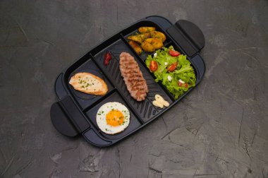 Kahvaltı bifteği ya da pirzola, domatesli ve yeşil sebzeli salata, kızarmış ekmek, patates, yumurta, üstten manzara, koyu arka plan. Sağlıklı beslenme, beslenme, menü, besleyici gıdalar.