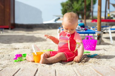 Deniz kenarında oyuncaklarla oynayan kız bebek