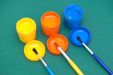 Üç paintbrushs ve farklı renklerde gouaches: sarı, turuncu, mavi