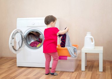 Küçük kız bir çamaşır makinesi yakınında giysi tutan