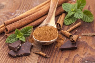 Bir tahta kaşık, nane yaprağı, tarçın ve koyu çikolata parçalarını toz tarçın.