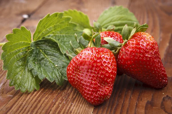 Ripe strawberries and strawberry leaves in a studio on wood.