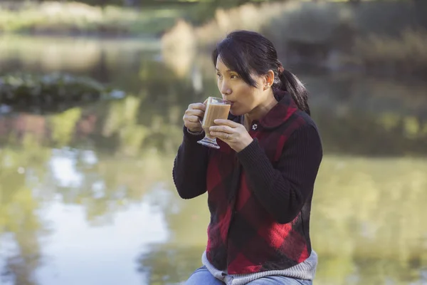 Frau trinkt ihren Kaffee am Teich. — Stockfoto