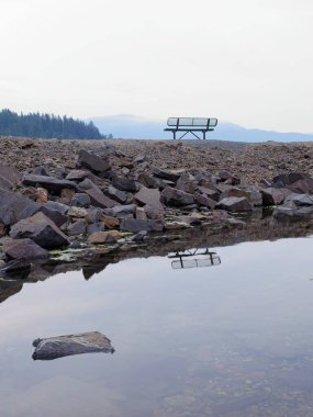 An empty metal park bench up on a path of land by Garfield Bay in Pend Oreille Lake in north Idaho. 