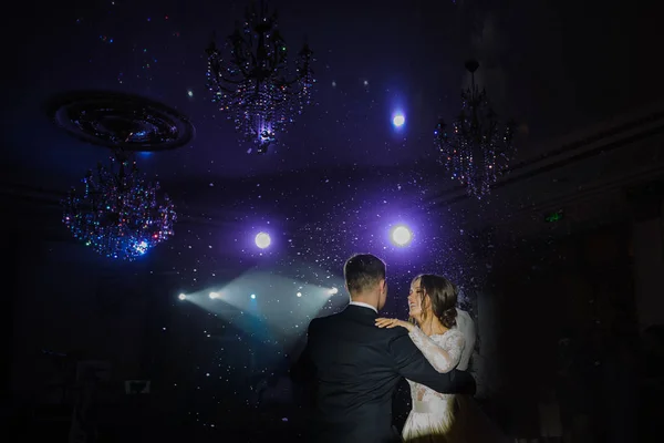 Beautiful first wedding dance of smiling, happy, bride and groom on low violet light and snow