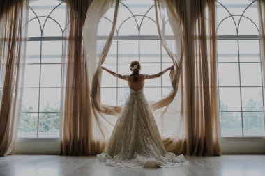 Uzun beyaz elbiseli güzel gelin pencereden dışarı bakar..