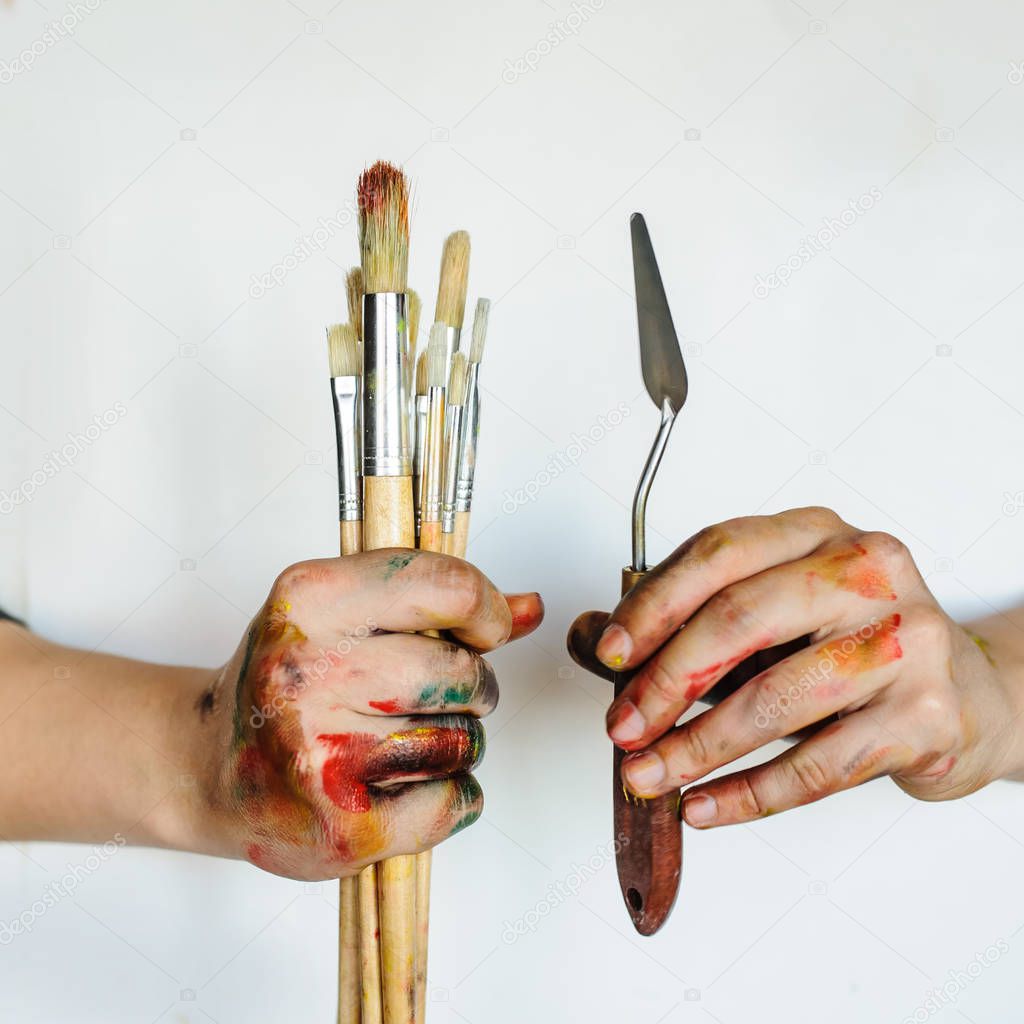 Close Up of an artist/painter hands holding paint brushes. Dirty painted with colorful paint on white background