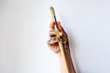 Eller yukarı yakın bir sanatçı/ressam boya fırçaları tutarak. Kirli beyaz arka plan üzerinde renkli boya ile boyanmış