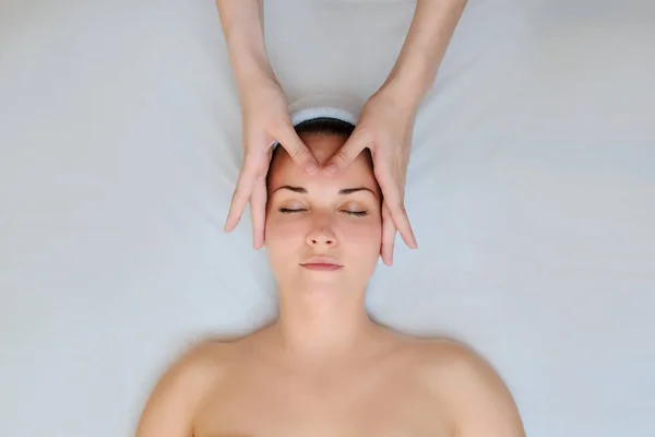 按摩脸部的水疗程序 顶部视图 美丽的年轻女子躺在背上 按摩师 治疗师按摩她的脸 — 图库照片