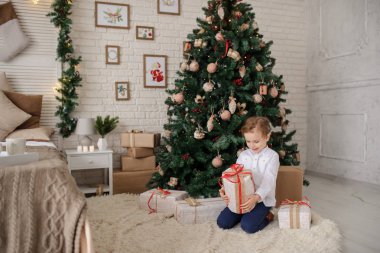 6 yaşında sarışın bir çocuk elinde hediyesiyle bir noel ağacı ve yatağının yanında