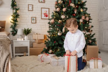 6 yaşında sarışın bir çocuk elinde hediyesiyle bir noel ağacı ve yatağının yanında