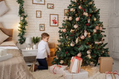 6 yaşında sarışın bir çocuk elinde hediyesiyle bir noel ağacı ve yatağının yanında