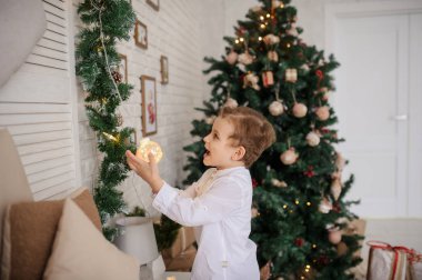 Noel ortamında elinde Noel ışıkları olan 6 yaşında sarışın bir çocuk.