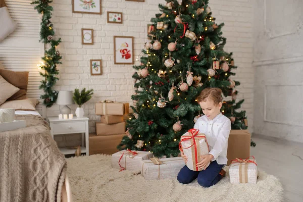 6 yaşında sarışın bir çocuk elinde hediyesiyle bir noel ağacı ve yatağının yanında