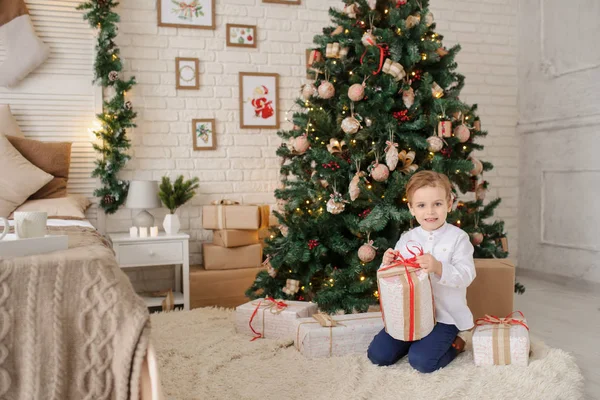 6 yaşında sarışın bir çocuk elinde hediyesiyle bir noel ağacı ve yatağının yanında